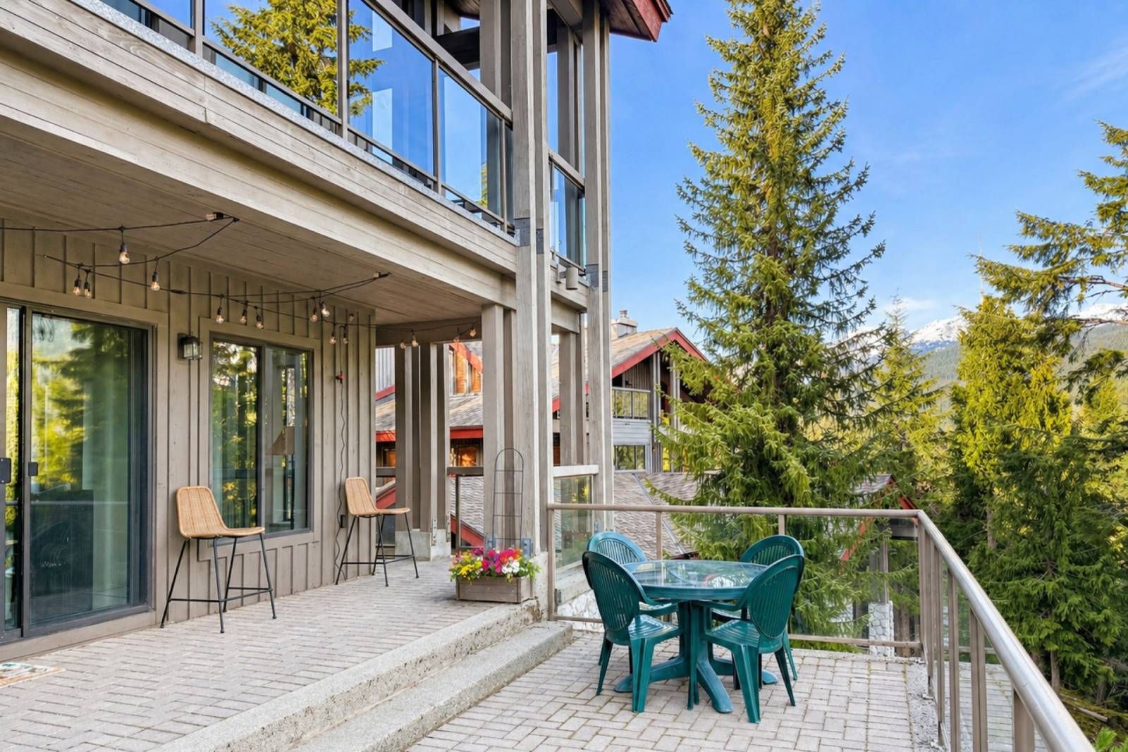 One of the two decks, set with a bistro table and string lights, looking out through evergreens to the mountains.