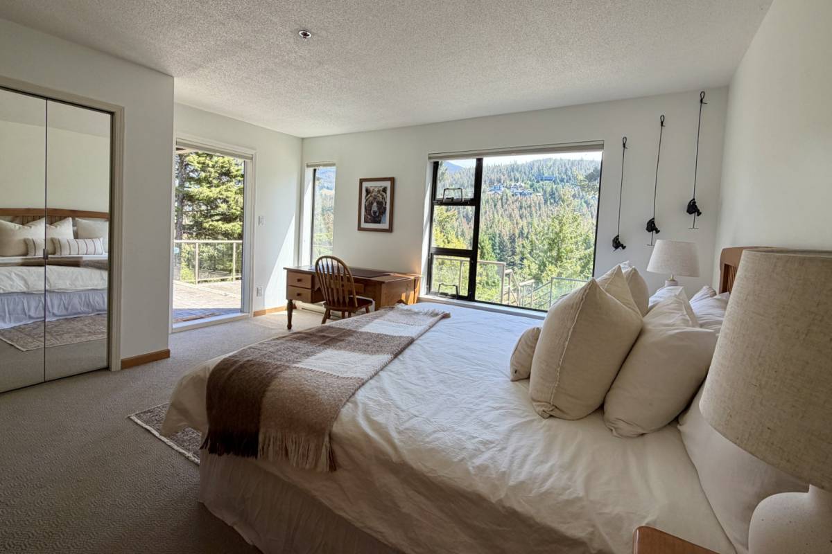 The master bedroom with a king bed, a mirrored closet, a small writing desk, and patio doors opening to a mountain view.