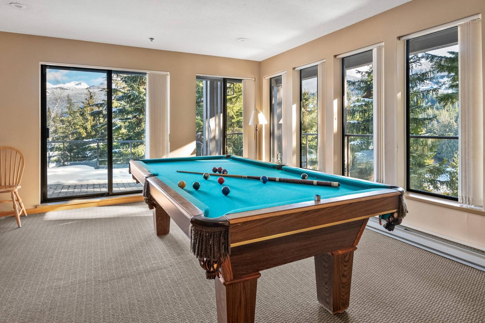 The games room with a pool table set up and floor-to-ceiling windows looking out to the mountains.